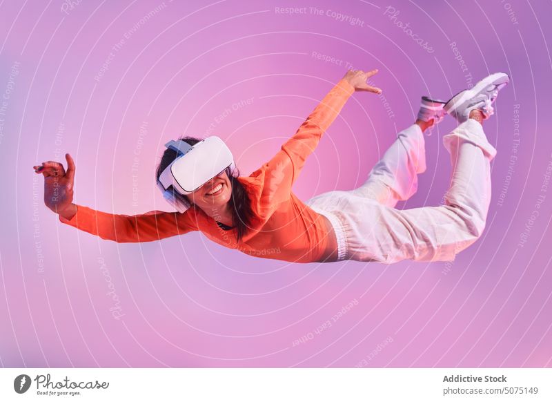 Woman in VR glasses suspended in the air woman vr fly fall concept explore experience futuristic immerse gesticulate female style colorful helmet headset