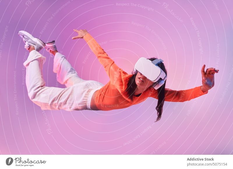 Woman in VR glasses suspended in the air woman vr fly fall concept explore experience futuristic immerse gesticulate female style colorful helmet headset