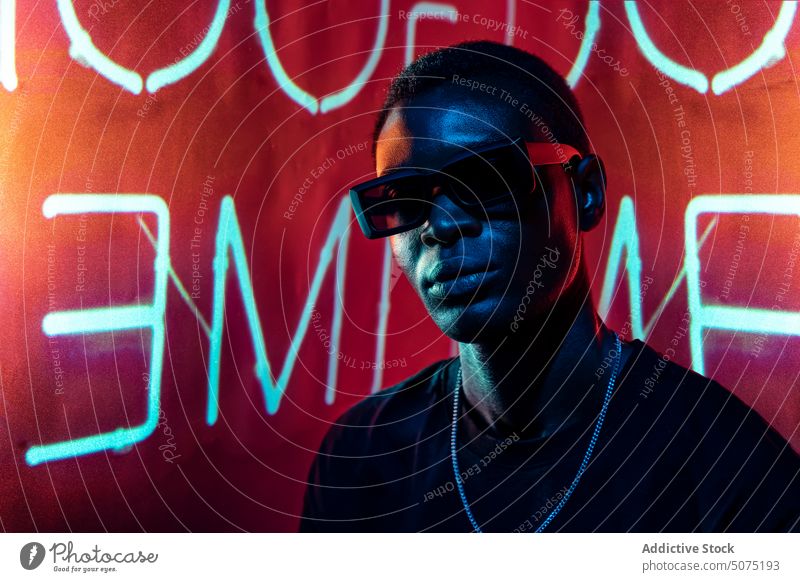 Cool black man in fashionable sunglasses in neon light cool metaverse confident ultraviolet nightclub luminous male letter glow nightlife modern bright trendy