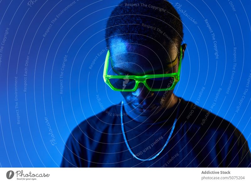 Black man in stylish sunglasses in neon light confident style metaverse self assured ultraviolet cool male young black man arms crossed masculine modern