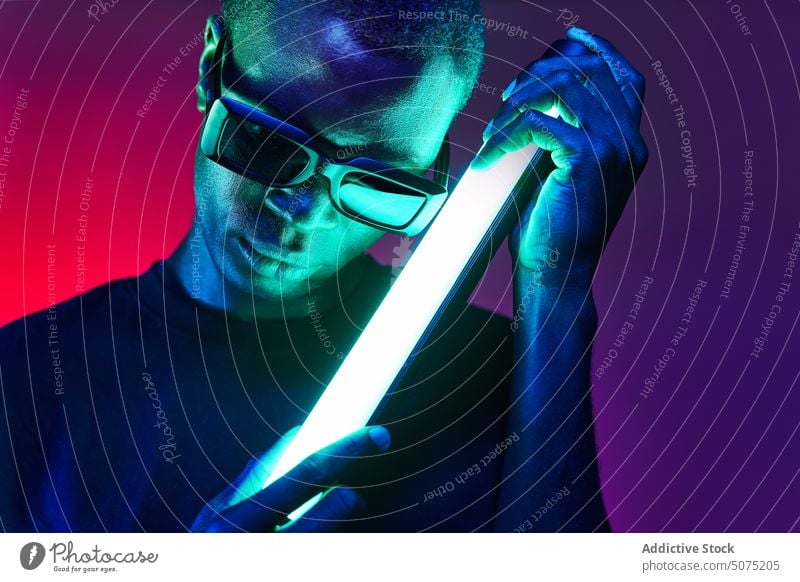 Extravagant black man in sunglasses with fluorescent lamp in hands extravagant metaverse reflect neon glow light chain male eccentric african american eyewear