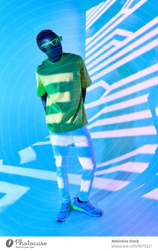 Cool black man in green T shirt and sunglasses posing in shadows cool effect pose stripe casual metaverse confident style bright light male young
