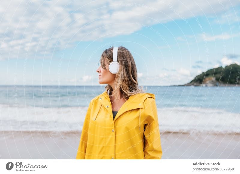 Woman in wireless headphones contemplating nature of beach woman contemplate warm clothes listen song relax sandy coast wavy foam seashore female
