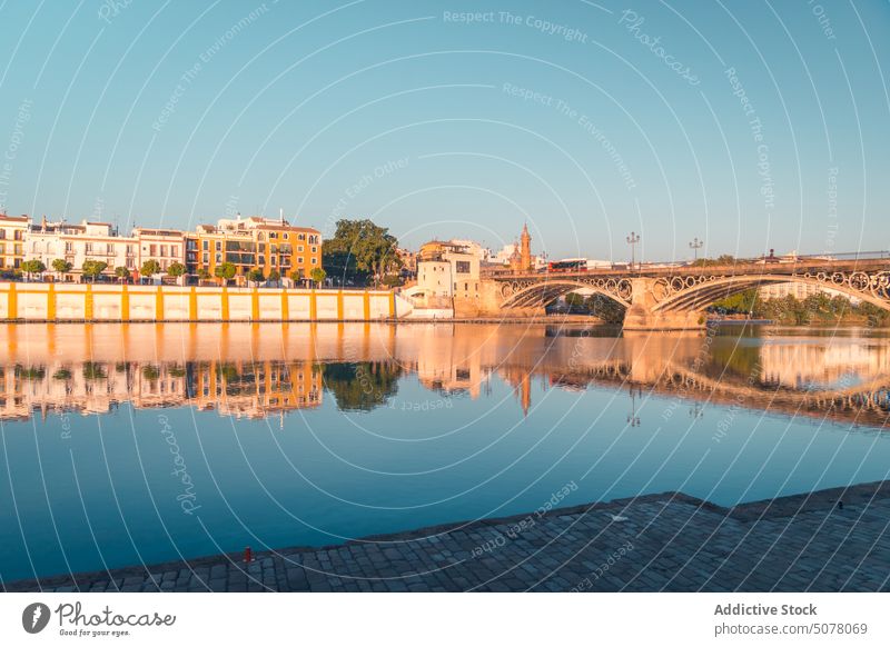 Old bridge over calm river with embankment of buildings in Seville seville exterior aged peaceful historic spain architecture andalusia old construction town