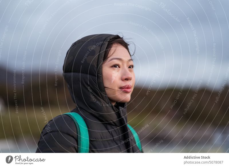 Dreamy Asian woman in warm clothes standing outside traveler hiker outerwear jacket rain cold weather trip weekend thoughtful positive young asian ethnic female