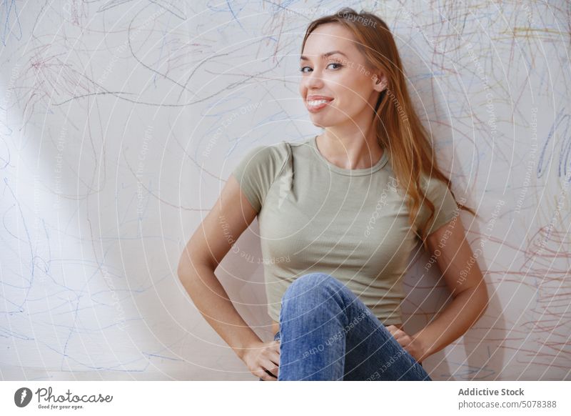 Smiling woman sitting against wall with scribbles rest mess mother meditate alone home tranquil smile positive calm colorful female happy lady young casual top