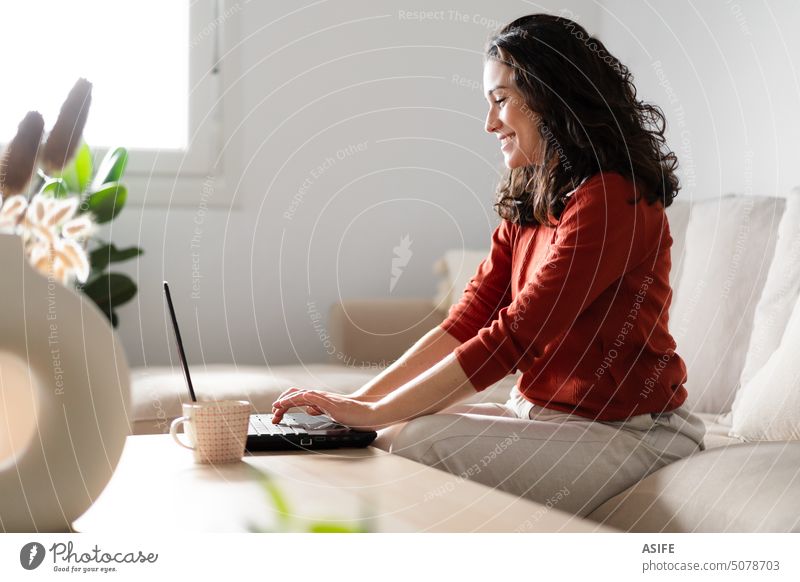 Happy young woman using laptop sitting on the couch home happy smiling online internet technology beautiful working computer business one people lifestyle