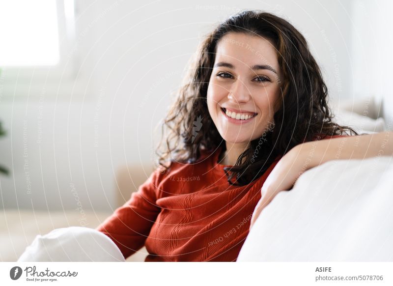 Portrait of a beautiful young happy woman relaxing sitting in the couch at home smiling toothy portrait looking at camera leisure relaxation smile comfort