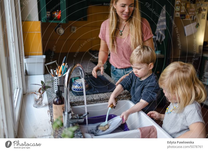 Children helping mother washing dishes in the kitchen real life real people bonding family indoors quality time house parenting kids enjoyment day parenthood