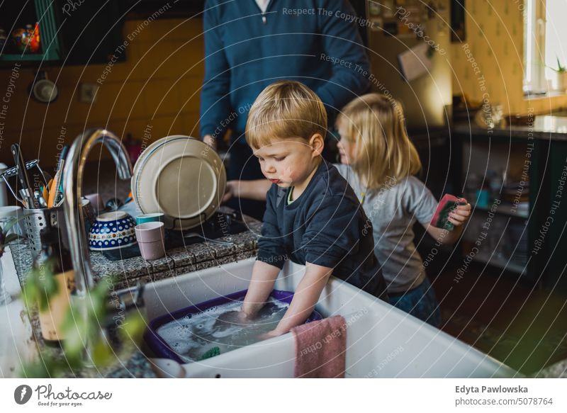 Children helping father washing dishes in the kitchen real life real people bonding family indoors quality time house parenting kids enjoyment day parenthood