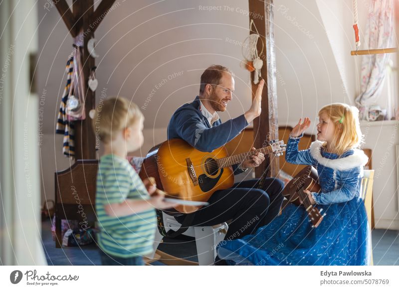 Dad teaching his kids how to play guitar modern manhood genderblend real life real people bonding family indoors quality time house parenting enjoyment together