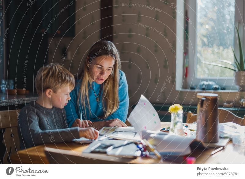 Mother helping son with homework at home real life real people bonding family indoors quality time house parenting kids enjoyment day parenthood together