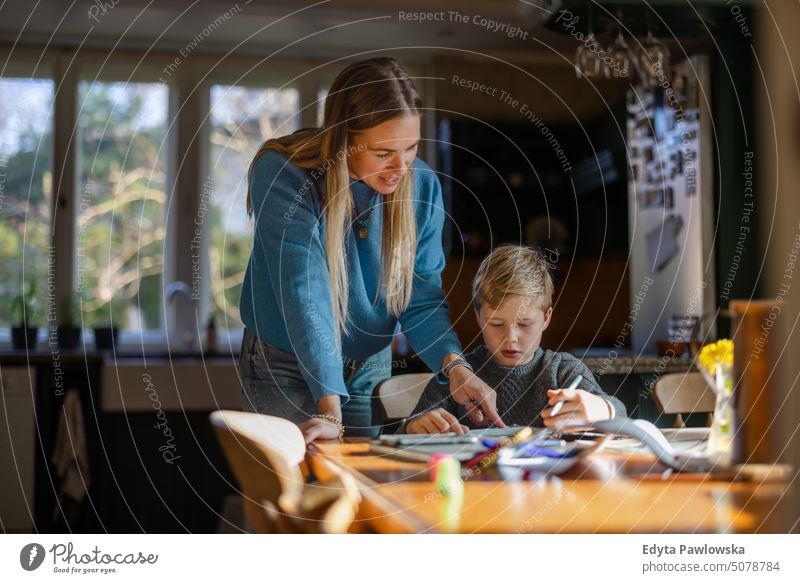 Mother helping son with homework at home real life real people bonding family indoors quality time house parenting kids enjoyment day parenthood together