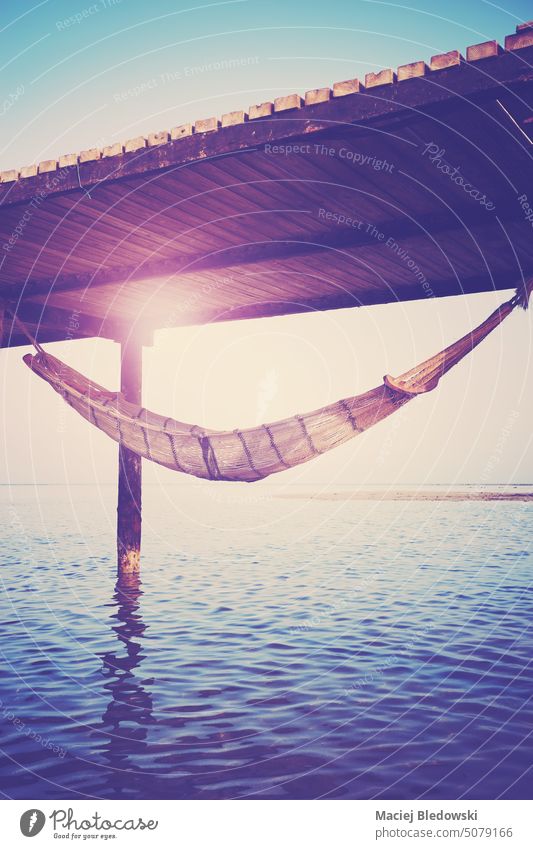 Empty hammock hanging under a sea wooden pier, getaway concept, color toning applied. vacation water beach sun summer travel paradise ocean tropical beautiful
