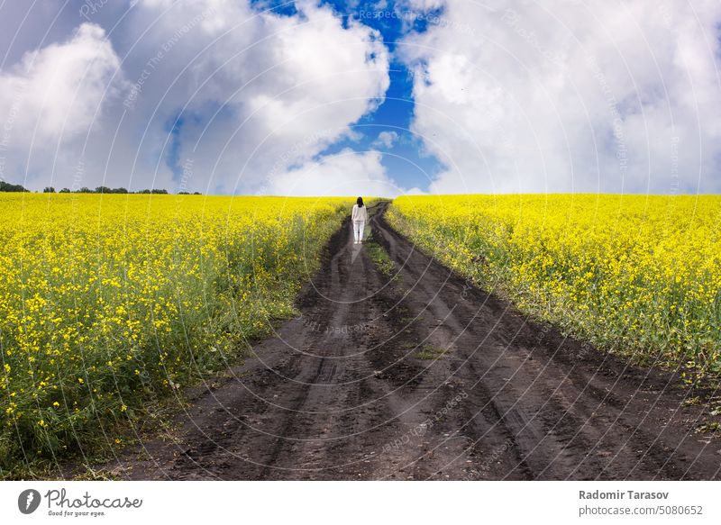 woman stands on a dirt road in a rapeseed field beautiful siberia russia summer season girl yellow nature beauty caucasian happy sunny female costume dreaming