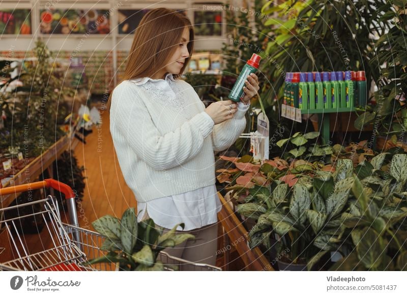 Young woman gardener buying plant care product in flower garden store indoors. bottle shop hold leaves tonic spray choose hand young smiling houseplant home
