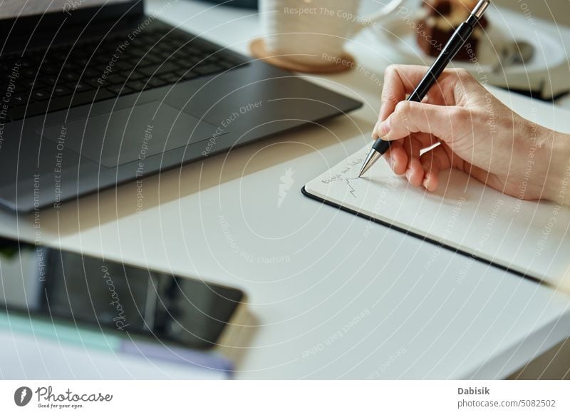 Designer draws sketch on paper, sits at desk with laptop in front of window woman work from home hand workplace creative remote freelance office workspace