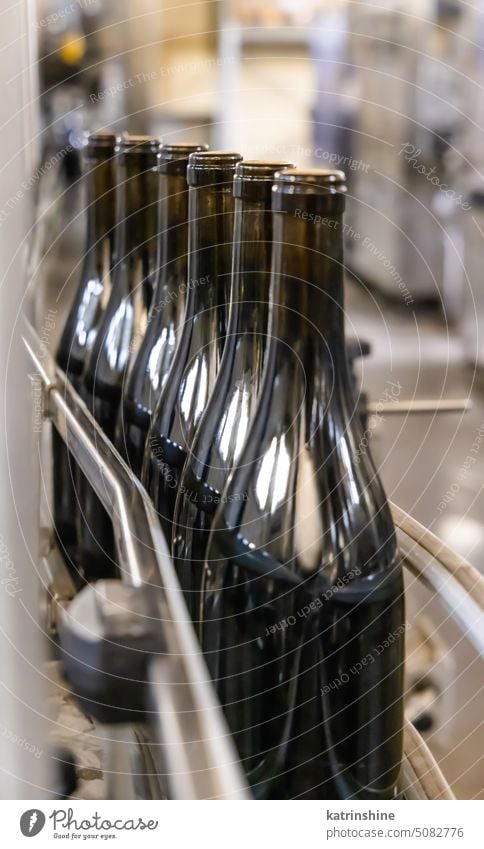 Dark glass bottles being filled with wine by industrial bottling machine at modern wine factory wine factoy italy wine-making conveyor winery automated filling
