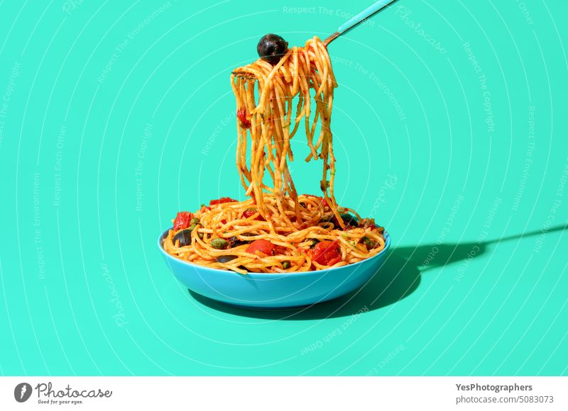 Eating spaghetti puttanesca from a bowl, minimalist on a green background blue bright capers carbs close-up color cooked copy space creative cuisine cut out