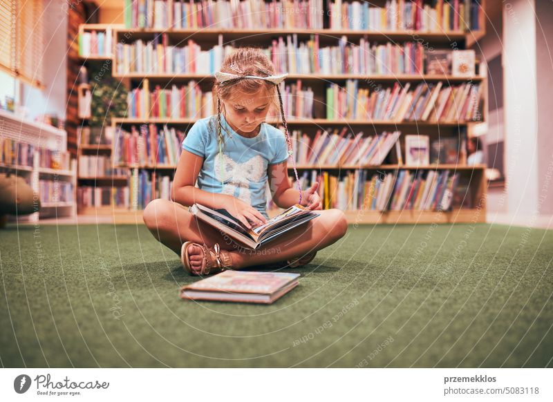 Primary schoolgirl doing homework in school library. Student learning from books. Pupil studying interesting books. Back to school back student child reading