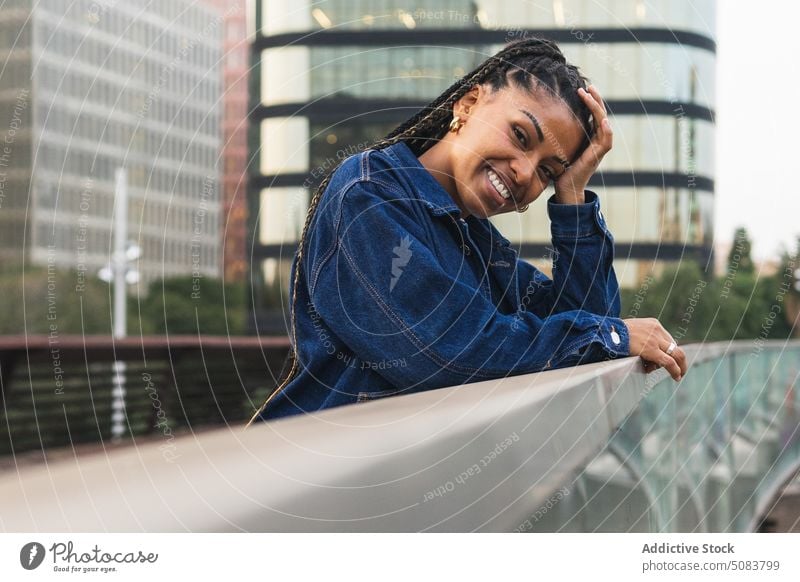 Cheerful black woman standing on bridge against urban traffic railing town cityscape building chill street smile positive happy african american ethnic female