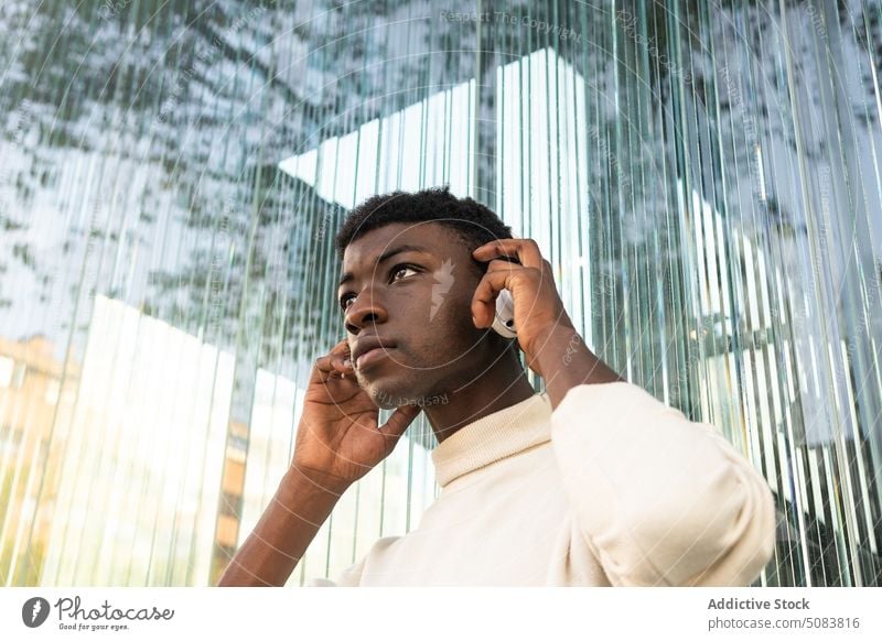 Black man with headphones near modern building listen music using wireless serious cool thoughtful gadget city male device playlist song urban casual young