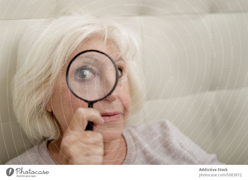 Senior woman with magnifying glass pensioner curious positive bed bedroom comfort magnifier interest warm clothes home senior blond inside female calm