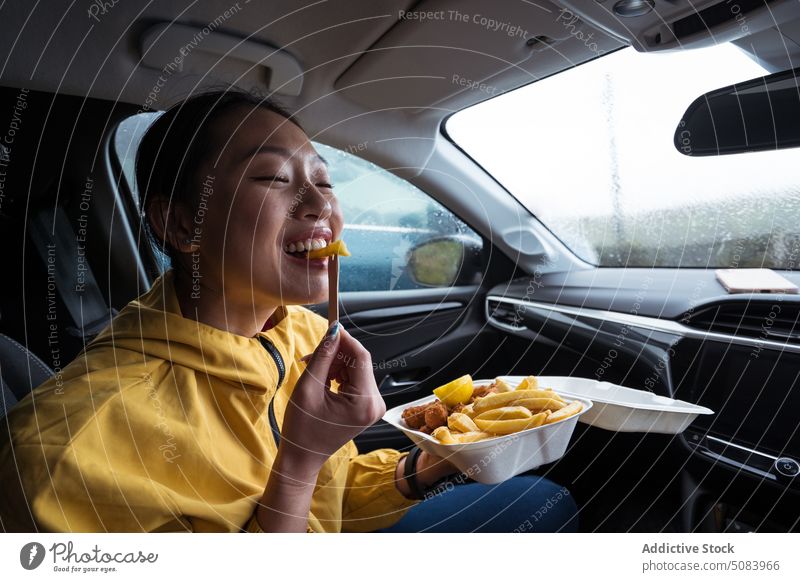 Asian woman eating chips in car fried potato wooden fork snack fast food rain female uk united kingdom cheerful asian ethnic scotland europe delicious fries