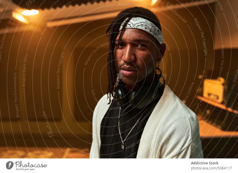 Black man with headphones on neck sitting in studio portrait musician record chill glow light pleasure personality male acoustic meloman song equipment stereo