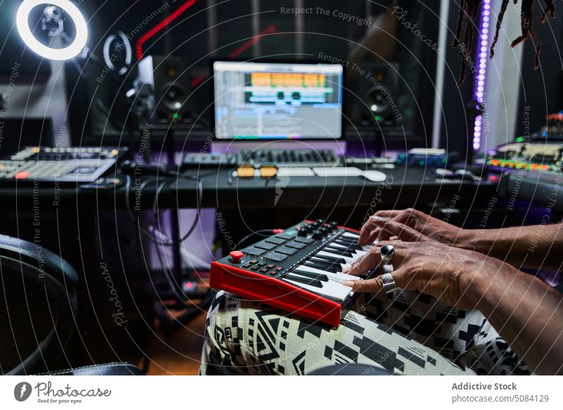 Anonymous black man playing synthesizer in modern recording studio musician talent rehearsal practice concentrate guy creative mixer computer column song melody
