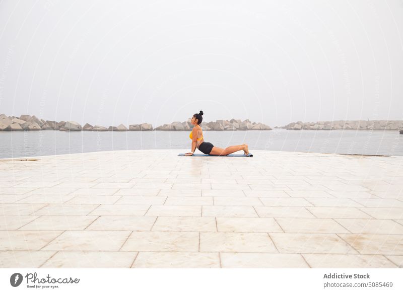 Sportive woman doing Cobra pose on mat near sea with stones yoga cobra pose bhujangasana workout sport exercise mindfulness concentrate endurance determine