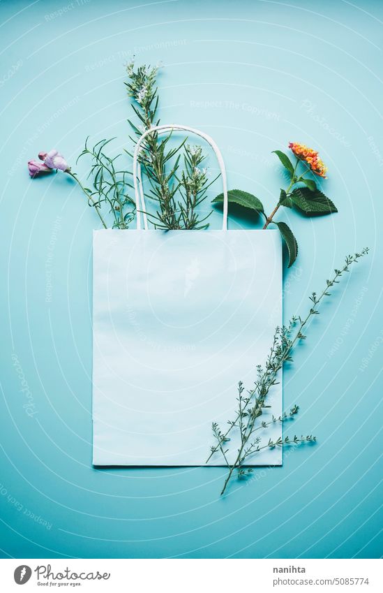 Seasonal mockup of a blue paper gift bag surrounded by flowers in flat lay format background spring nature natural organic wild floral decor bouquet herbs