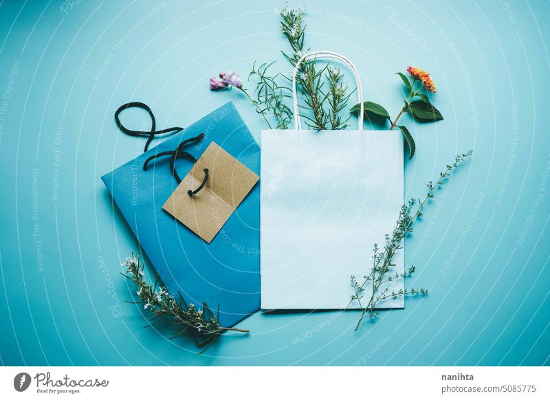 Seasonal mockup of a blue paper gift bag surrounded by flowers in flat lay format background spring nature natural organic wild floral decor bouquet herbs