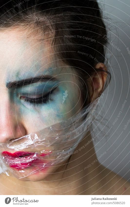Woman with crazy makeup and plastic wrap on mouth unusual Intensive variegated Strange Asphyxiate avant garde Apply make-up smudged plastic foil Model