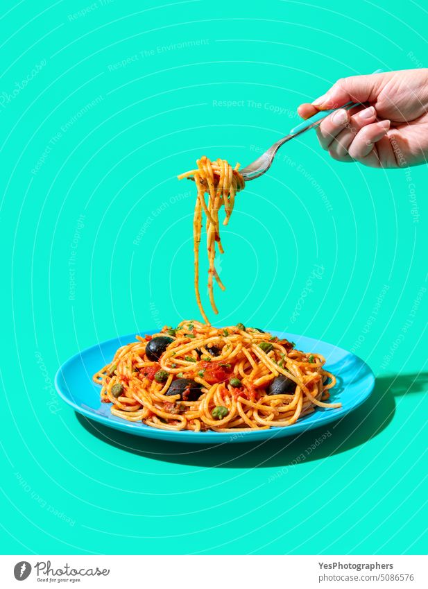 Pasta puttanesca plate minimalist on a green background. Eating vegan pasta. blue bright capers carbs color cooked copy space creative cuisine cut out delicious