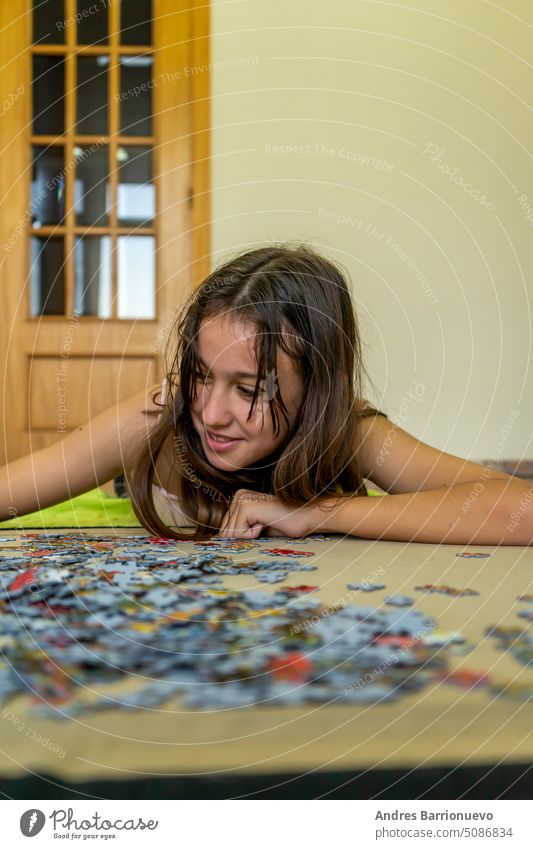 Teenage brunette girl doing puzzle lying on the floor of her house, she spends time running away from technology and enjoying traditional games. years caucasian