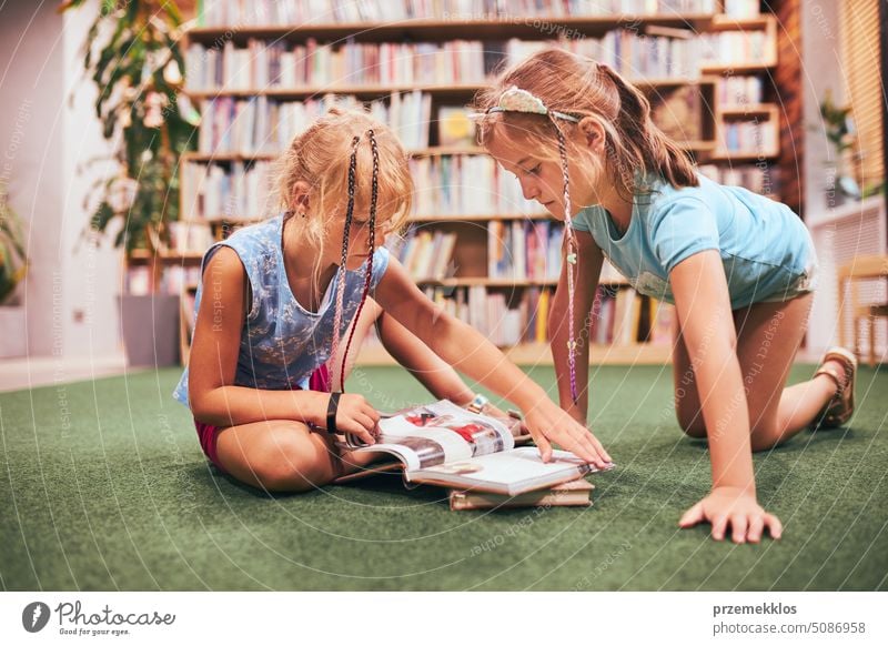 Two schoolgirls reading books in school library. Primary school students learning from books. Pupils doing homework. Children having fun in school club. Back to school