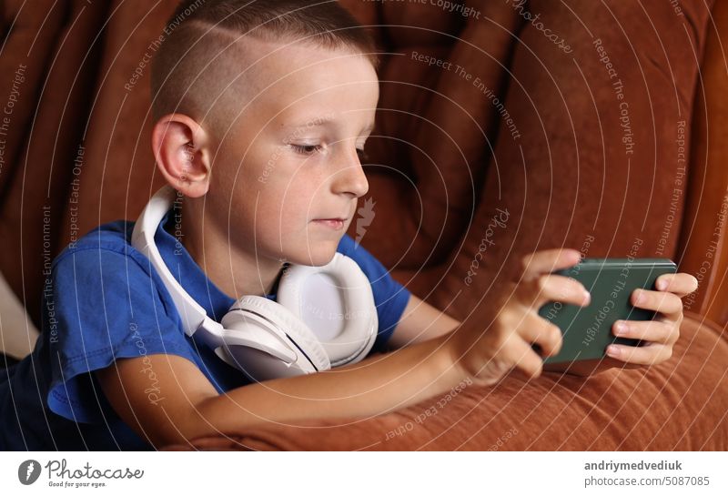 close up of child boy playing video games In smartphone at home on couch. Kid using phone for gaming online education social media. Schoolboy is studying game on mobile phone.