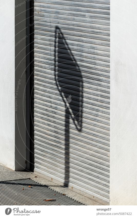 Shadow of a sign falls on the closed blind of a rolling gate Venetian blinds Rolling door Entrance Closed Building Goal sunshine Exterior shot Deserted