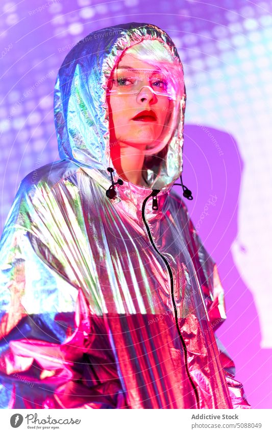 Woman in silver jacket looking at camera woman model neon illuminate futuristic contemporary studio shot glow emotionless unemotional female transparent goggles