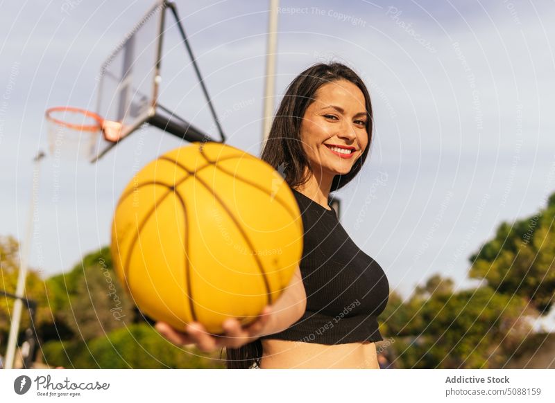 Smiling woman with orange ball on court player streetball show hoop game hobby sport activity cheerful smile sporty sportswoman energy demonstrate athlete