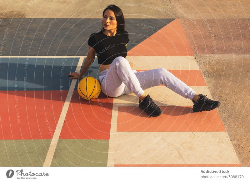 Fit female sitting on ground with basketball during basketball training woman break lean back court relax streetball hobby sporty slim sportswoman rest athlete