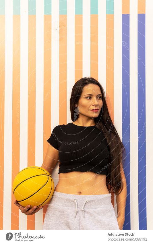 Pensive woman standing against striped wall with basketball ball sportswoman wellness hobby leisure physical player motivation sporty fit joy slim pensive