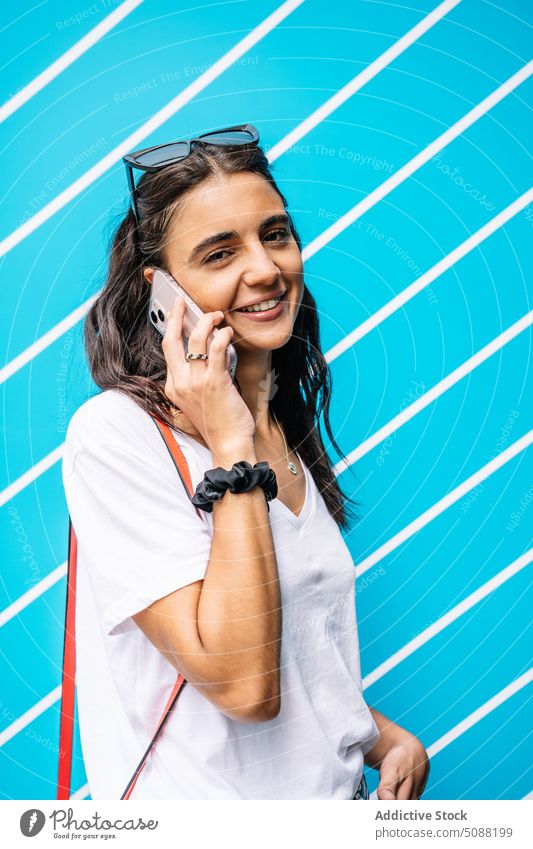 Happy woman talking on smartphone near wall with lines happy cheerful conversation mobile smile female young speak gadget communicate glad phone call positive