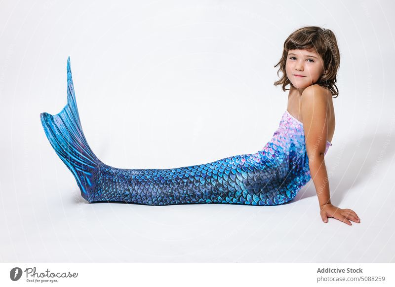 Charming girl sitting in studio in mermaid costume kid tail scale shimmer creative fantasy festive smile cheerful joy adorable little child childhood blue