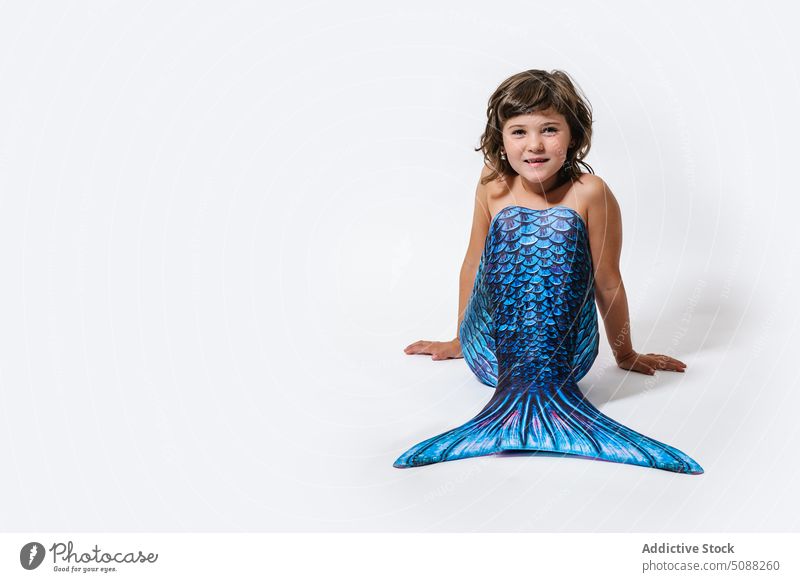 Charming girl sitting in studio in mermaid costume kid tail scale shimmer creative fantasy festive smile cheerful joy adorable little child childhood blue