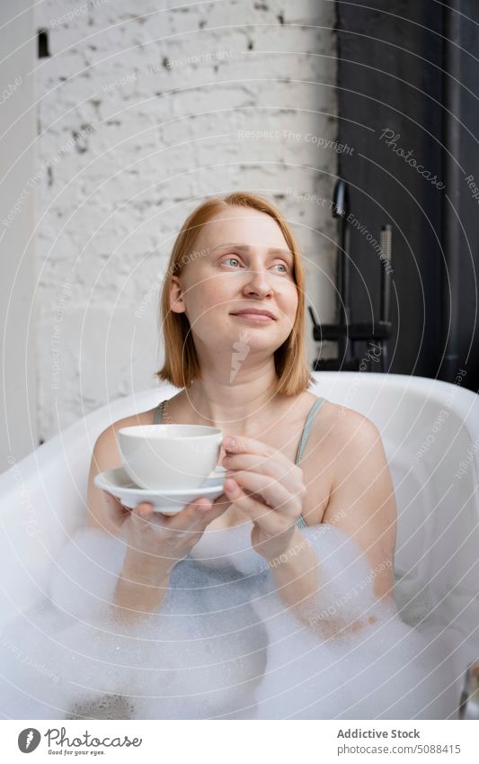 Woman chilling in bathtub with cup of drink woman relax foam hot drink saucer routine bathroom hygiene dreamy smile female daily refreshment beverage tea mug