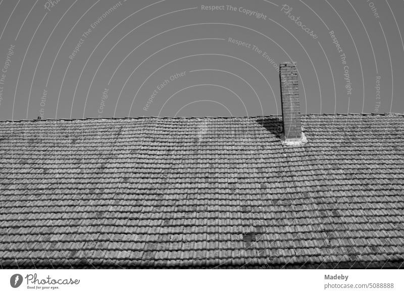 Crooked and wavy old tiled roof with brick chimney of a half-timbered house in the sunshine in the old town of Blomberg near Detmold in East Westphalia-Lippe, photographed in neo-realistic black and white