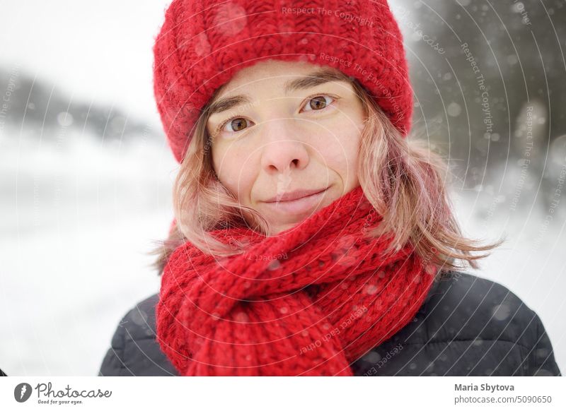 Close-up portrait of young beautiful caucasian woman with pink hair wearing red hat and scarf during snowfall on winter day. cute clothes adult airing