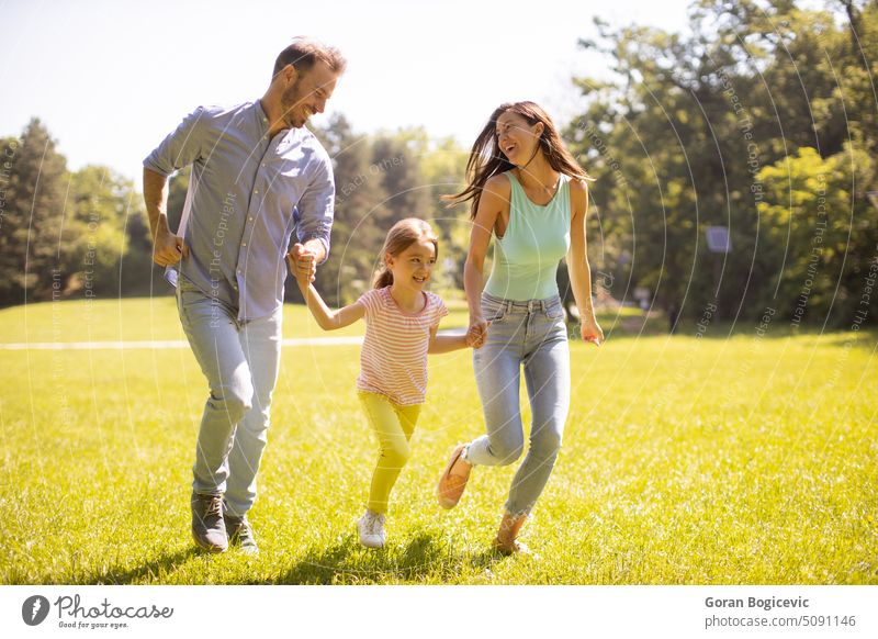 Happy young family with cute little daughter having fun in the park on a sunny day adult back beautiful caucasian cheerful child childhood couple dad enjoyment